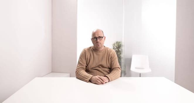 sad bald plump man with glasses in an empty office waiting for something that have to happen