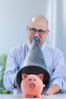 piggy bank on the foreground and shouting man with a megaphone on the background with strong difference of focus
