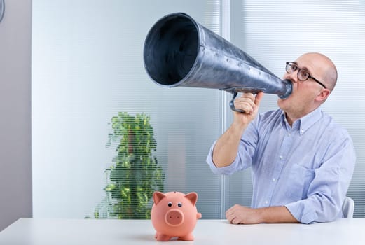 a bald office worker shouts in a megaphone talking about savings represented by a piggybank on the desktop