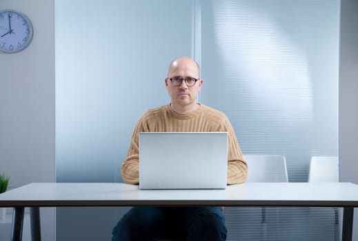 office worker with a nerd attitude and an open laptop on the top of an empty desktop in an almost empty room waiting for you to act
