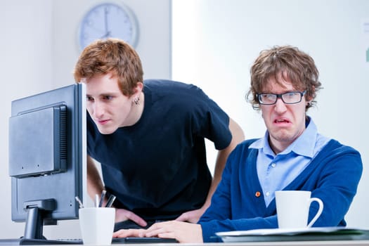 a disgusted office worker while the other one looks for something in a computer screen