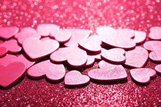 Lots of small pink wooden hearts on a red glitter background
