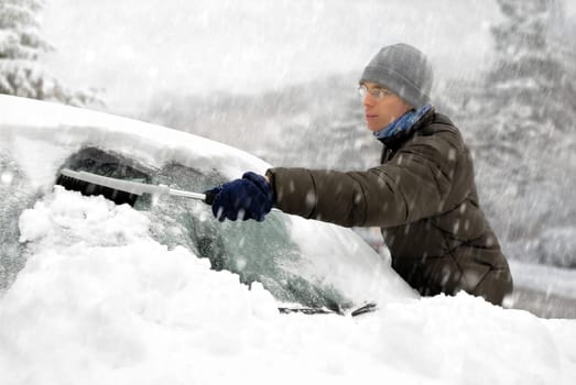 Young man removes the snow from his vehicle