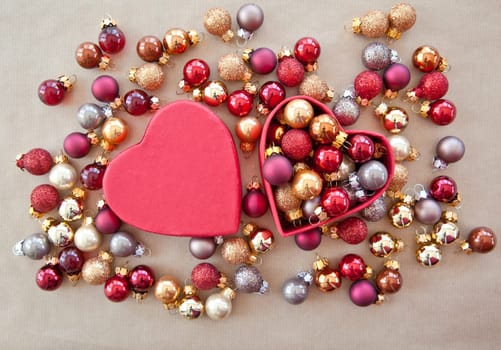 Red heart box with colorful Christmas tree balls on wrapping paper