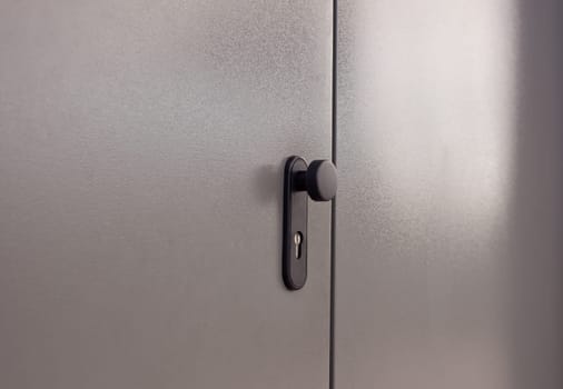 Black doorknob over isolated grey background of the door, outdoors side
