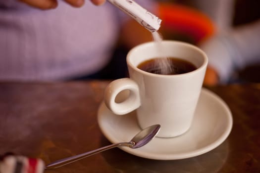 Adding sugar to his white ceramic cup on restaurant terrace table. Selective focus