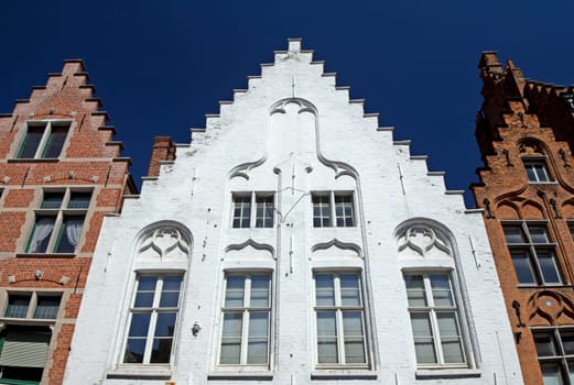 Historic houses in the center of Bruges (Belgium). Front view. White house between two red houses.