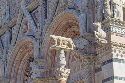 Closeup view of the gothic Cathedral of Siena. Next to the façade stands a column with a statue of the Contrade Lupa, a wolf breast-feeding Romulus and Remus (Tuscany, Italy)