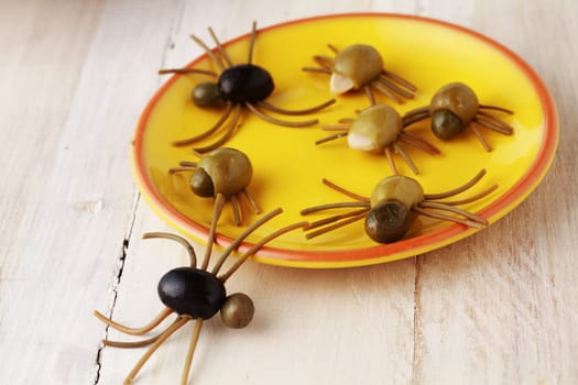 Creepy crawly Halloween spider snacks for a party celebration made from black and green olives with Italian spaghetti legs served on a yellow plate on a rustic white wooden table