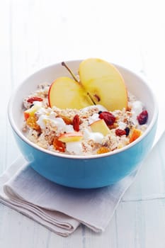 Bowl of healthy breakfast cereal with a halved fresh apple and topped with diced apple, dried fruit and nuts served with milk in a blue ceramic bowl, high angle view
