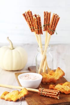 Rustic appetizers for a Halloween party with Witches broomsticks made from bread sticks and pretzels and bat cookies or biscuits served with a savory dip with a white autumn pumpkin behind