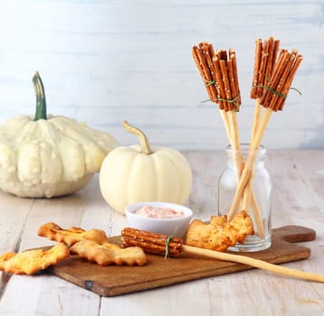 Fun homemade rustic Halloween witches broomstick appetizers made from bread sticks and pretzels served on a wooden board with a savory dip and bat biscuits