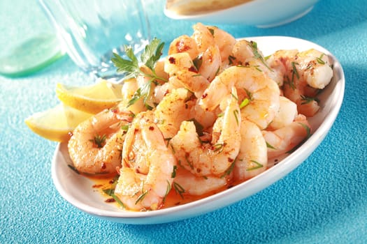 Dish of grilled shelled pink prawns seasoned with virgin olive oil and diced herbs and garnished with slices of lemon served as a seafood appetizer to a meal
