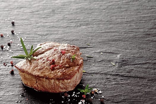 Tender medallion of lean grilled fillet or rump steak seasoned with salt and peppercorns and garnished with fresh rosemary on a griddle with copyspace