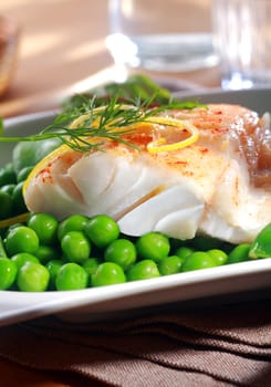 Delicious seafood meal of grilled or oven-baked fish fillet served with juicy green petit pois peas , lemon zest and dill at a restaurant