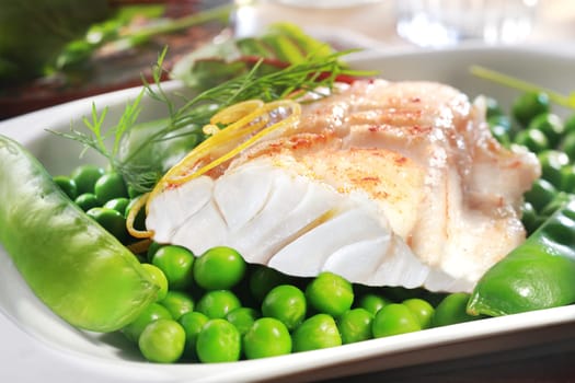 Healthy grilled fish steak with peas, mangetouts and lemon zest served on a plate as an appetizer or main course