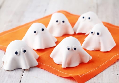 Scary white edible Halloween ghost appetizers for party snacks or treats for young children trick-or-treating on Allhallows Eve standing ready on a colorful orange napkin