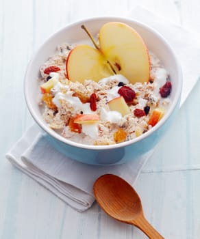 Delicious homemade muesli with fruit including fresh halved and diced apple and dried apricots and raisins and nuts served in a bowl on a white wooden rustic table