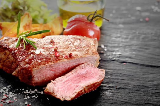 Healthy trimmed lean medallion of grilled rare rump steak sliced through to show the texture seasoned with salt and herbs on an old wooden surface with ingredients and copyspace