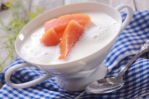 Bowl of gourmet chowder with raw salmon pieces in a frothy broth in an elegant white china bowl over a blue and white checked napkin