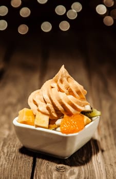 Tangy orange, mandarine or tangerine citrus frozen yogurt with fresh fruit salad in a owl on a rustic wooden table with copyspace and a bokeh of sparkling party lights