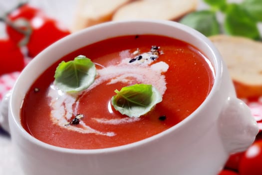Bowl of delicious homemade tomato soup with cream and basil seasoned with pepper, closeup view