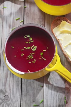Red Violet Beetroot Soup in Yellow Pot, Perfect for Bread with Spread, Placed on Vintage Wooden Table.