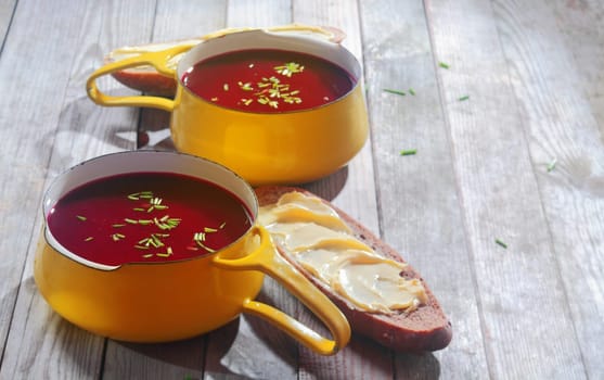 Beetroot Soups on Yellow Bowls with Handle and Bread with Spread Placed on Wooden Tables.