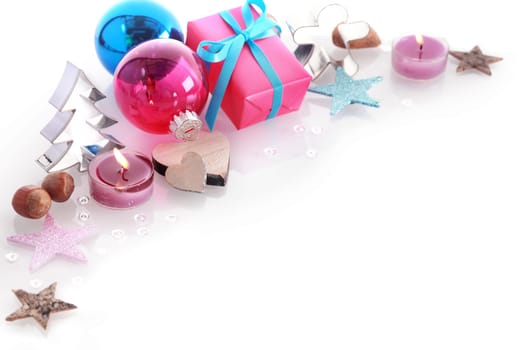 Colorful Christmas still life with blue and red baubles, gift , burning candles, stars, nuts and a Christmas tree shaped cookie cutter over white with copyspace for your Xmas greeting