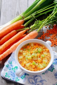 Nutritious lentil, carrot and leek soup served in a bowl surrounded by fresh bunches of carrots, leeks and dried orange lentils
