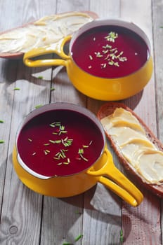 Appetizing Beetroot Soup in Yellow Bowl with Handle, with Sliced Bread on Sides Placed on Wooden Table.