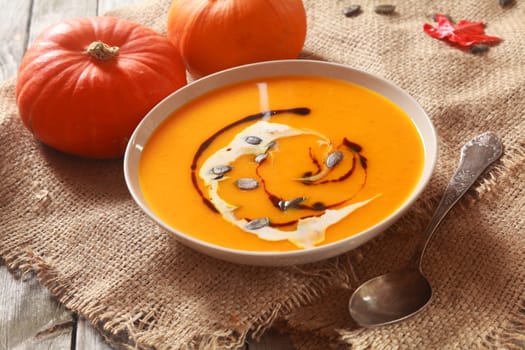 Bowl of delicious hot fresh homemade pumpkin soup with ingredients on a square of rustic hessian in a country kitchen