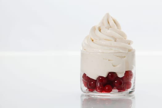 Ripe redcurrants topped with vanilla frozen yogurt served as a party dessert in a glass dish on a white table with copyspace