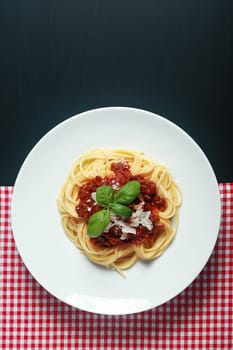 Gourmet Italian Pasta Food on White Round Plate Placed Between Red White Checked and Black Background.