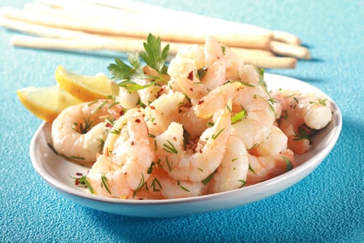 Grilled pink shelled marine prawns seasoned with olive oil and herbs served with lemon and bread sticks for a tasty seafood starter to dinner, on turquoise blue