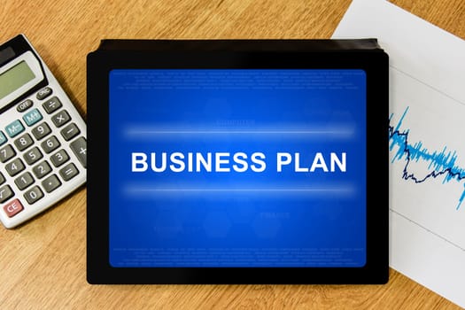 business plan word on digital tablet with calculator and financial graph