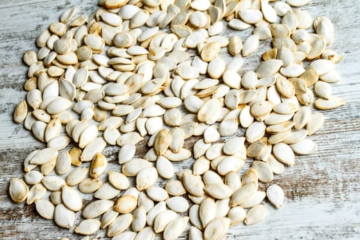 Many pumpkin seeds on a wooden table, background.