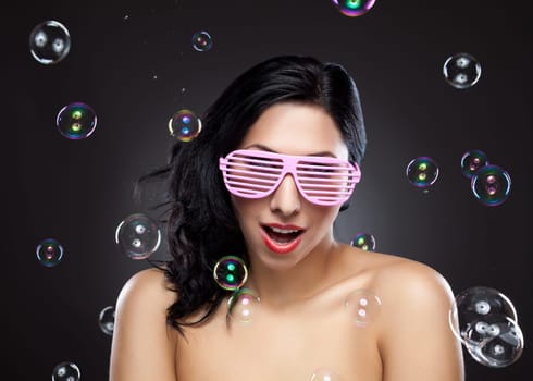 Young and happy woman wearing pink glasses surrounded by bubbles