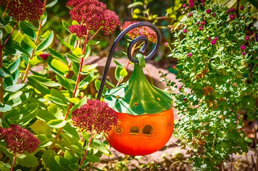 Handmade ceramic jack-o'lantern between the plants in the garden.