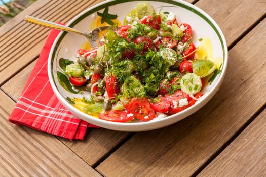 Bowl of marinated Greek salad with tomato cheese and olives on a wood edible