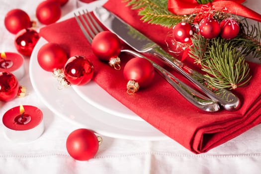 Red napkin with Christmas glass balls and cutlery with a green fir branch and red bow close-up