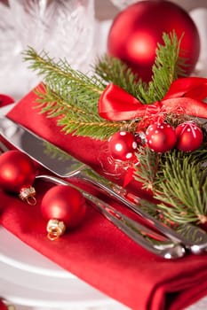 Red napkin with Christmas glass balls and cutlery with a green fir branch and red bow close-up