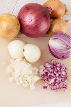White and red onions peeled and with slurs as a whole and in cubebrunoise as a close-up on cutting board