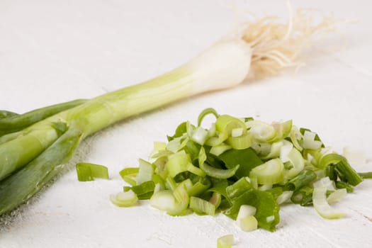 Leek spring onions with root as a whole and cut as a close-up on a white wooden board