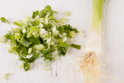 Leek spring onions with root as a whole and cut as a close-up on a white wooden board