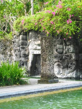 Detail of a pool in Bali with small cave and religious symbols.