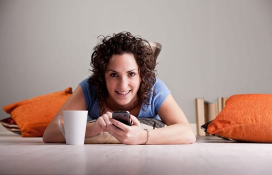 girl texting with her smartphone drinking a hot drink from her white mug