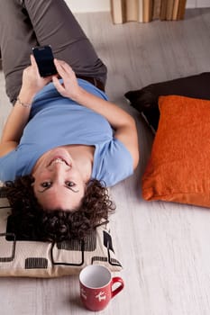 A smiling girl staring at camera with a mobile phone in her hands lying on the floor of her room