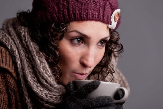 it's winter and this girl with wool hat and scarf drinks a hot chocolate or hot tea or milk from a big mug and she's happy
