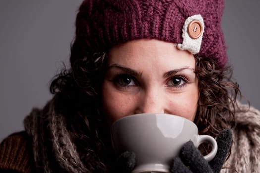 it's winter and this girl with wool hat and scarf drinks a hot chocolate or hot tea or milk from a big mug and she's happy